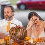 A bride and groom celebrating their wedding at a reception table adorned with pumpkins.