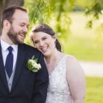 A wedding portrait of a smiling bride and groom in front of a tree.