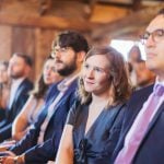 A group of people sitting in a row during a wedding ceremony in a barn.