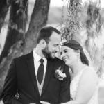 A black and white portrait of a bride and groom in front of a willow tree.