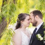 A wedding couple embraces under a willow tree.