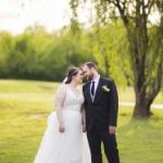 A portrait of a wedding couple kissing in front of a tree.