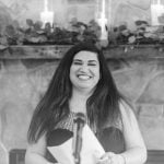 A woman smiles as she reads a speech at a wedding ceremony.