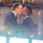 Two men sharing a wedding kiss in front of a mirror.