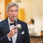 A man in a tuxedo speaking at a wedding reception.