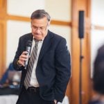 A man in a suit speaking into a microphone at a wedding reception.