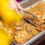 A person pouring gravy over chicken in a pan at a wedding.