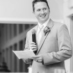 A black and white photo of a groom giving a speech at a wedding reception.