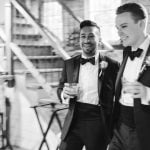 Two groomsmen in tuxedos walking down the aisle at a wedding reception.