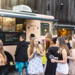 A group of people celebrating a birthday party or quinceanera standing in front of a food truck.