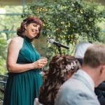 A woman in a green dress is giving a speech at a wedding reception.