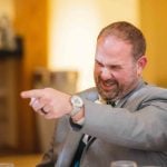 A man in a suit is pointing at a table at a wedding reception.