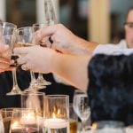 A group of people toasting wine glasses at a wedding reception dinner party.