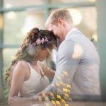 A wedding couple hugging in front of a window at their reception.