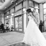 A bride and groom standing in front of a large reception room.