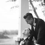 Two men in tuxedos sitting on a porch for a wedding portrait.