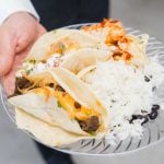 A man showcasing wedding details, holding a plate of tacos and rice.