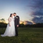 A wedding portrait of a bride and groom kissing in a field at sunset.