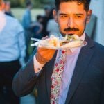 A man with a mustache holding a plate of food at a wedding.