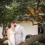 A wedding portrait of a bride and groom kissing in front of a tree.