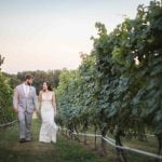 A wedding couple poses for a portrait in a vineyard at sunset.