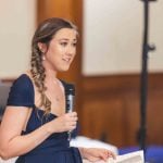 A woman in a blue dress speaking into a microphone at a wedding reception.