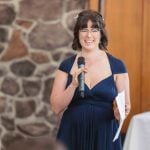 A woman in a blue dress giving a speech at a wedding reception.