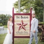 A wedding couple posing in front of a sign at the barns winery.