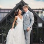 A wedding portrait of a bride and groom standing in front of a greenhouse.