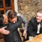 A group of groomsmen hugging each other at a wedding reception.