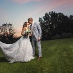 A newlywed couple having their wedding portrait taken in the grass at sunset.