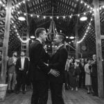 A black and white photo of two men sharing a wedding dance in a barn reception.