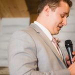 A man in a suit speaking into a microphone at a wedding reception.