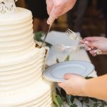 A person cutting a wedding cake at the reception.