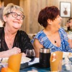 A group of women laughing at a dinner table during a Birthday Party gathering.