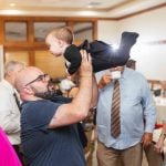 A man lifting a baby at a wedding reception.