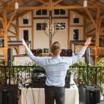 A dj at a wedding reception in a barn with his arms up.