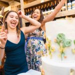 Two women cutting a birthday cake in a wine cellar.