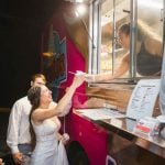 A bride and groom enjoying a food truck at their wedding reception.