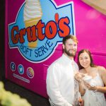 A bride and groom pose in front of a weddingthemed ice cream truck at their reception.