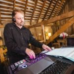 A man playing a DJ at a wedding reception in a barn.