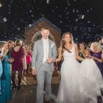 A bride and groom exiting a church after their wedding with bubbles thrown at them during their reception.