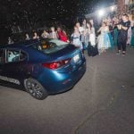 A group of people standing around a car at night during a wedding reception.