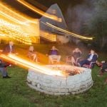 A wedding reception with people sitting around a fire pit at night.