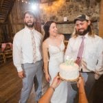 A wedding couple holding a cake during their reception in a barn.