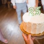 A woman is holding a wedding cake with the number 25 on it.