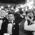 A black and white photo of groomsmen holding sparklers at a wedding reception.