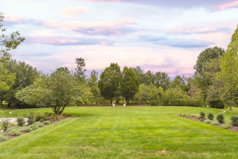 A large lawn with pleasant trees and bushes in the background near Pleasant Hill House.