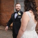 A bride and groom sharing a candid moment at their wedding in front of the historic brick building at Savage Mill.