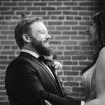 A candid bride and groom share a heartfelt moment in front of a brick wall at their wedding venue, Savage Mill.